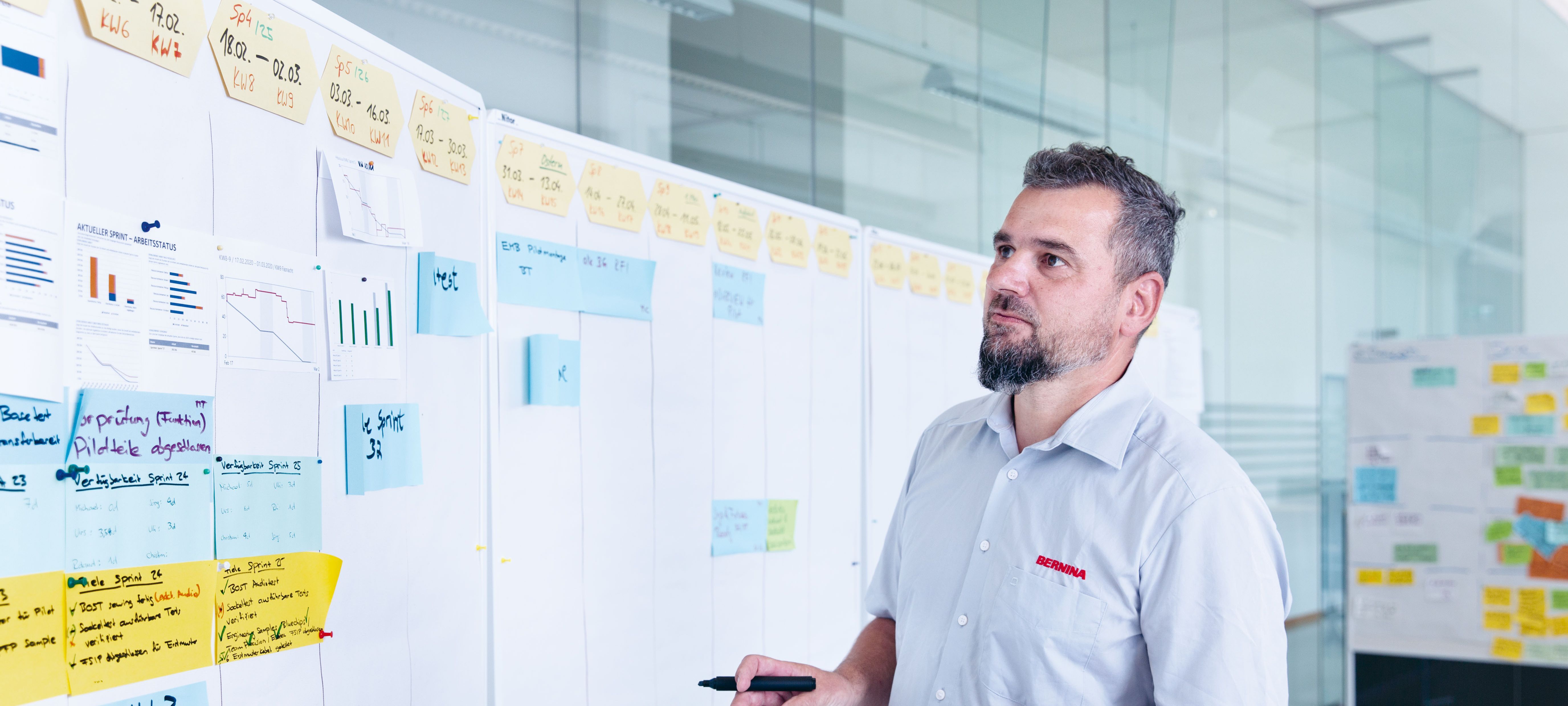 Ein Arbeitnehmer, welcher eine Weiterbildung im Projektmanagement bei der Swissmem Academy absolviert hat, vor einer Wand mit unterschiedlichen Grafiken, Post-Its und weiteren Informationen.